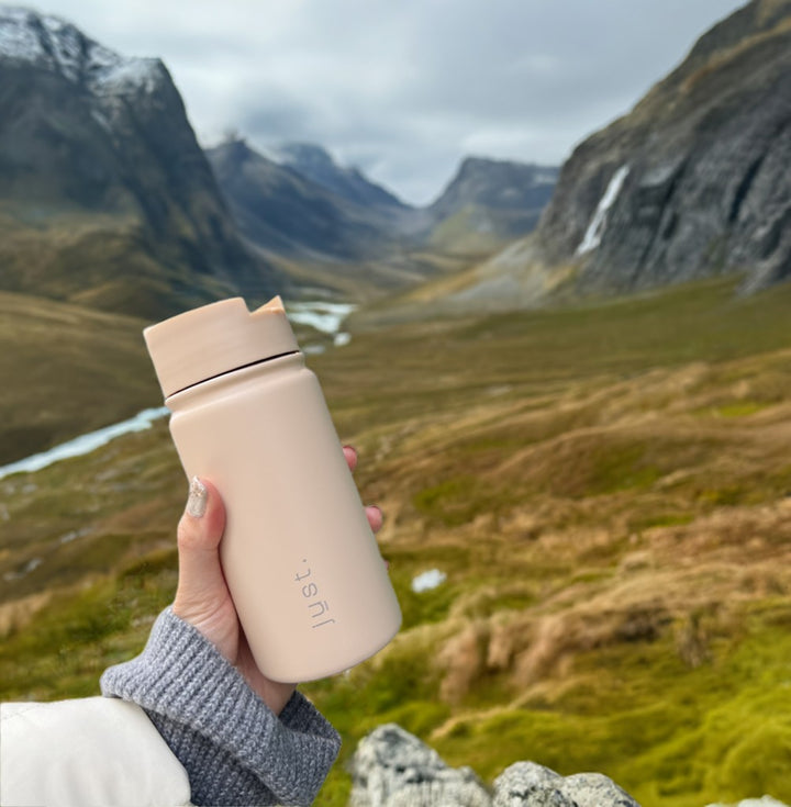 beige reusable coffee cup with green grass and nature background